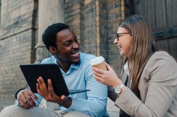 Smiling business colleagues using tablet and drinking coffee outdoors
