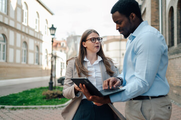 Businesspeople using tablet and laptop, discussing work outdoors