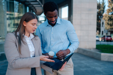 Business colleagues discussing work on laptop outside office building