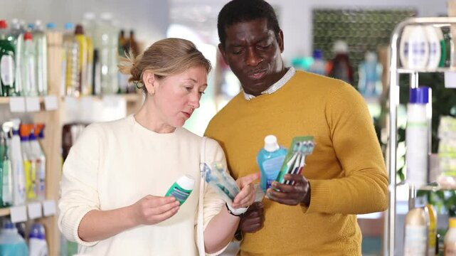 Couple collecting set of hygiene products for oral care. African man and European wife decided to buy dental care kit and looking for something in window, trying to find remedy for gum care