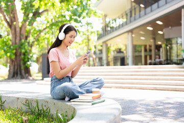Smiling student   listening to favorite radio station  holding smart phone sitting outdoors in...