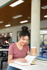 Female student sitting in cafeteria, reading book, studying for final exam at university.