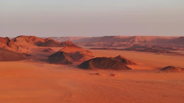 Stunning aerial view of the rocky desert landscape in southern Morocco during sunset, with warm orange light painting the mountains and casting shadows across the arid terrain
