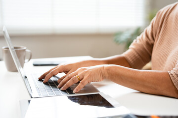 Close up on elderly woman hands using laptop typing on keyboard sitting at desk, senior asian lady...