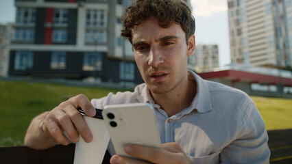 Shocked dissatisfied Caucasian young man holding cup of coffee user mobile phone smartphone male...