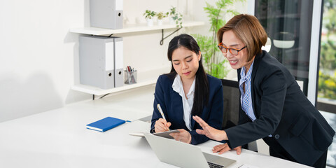 Confident mature business professional woman talking to younger female colleague at office table,...