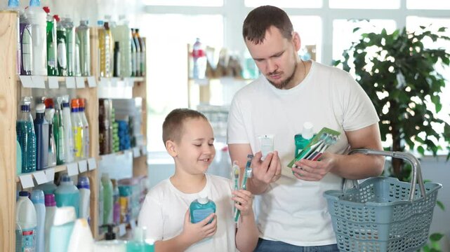 Buyers picked up oral care products. Dad and son took toothpaste, toothbrush, and mouthwash from shelf of showcase and are looking for additional remedy for gum health.  - Powered by Adobe