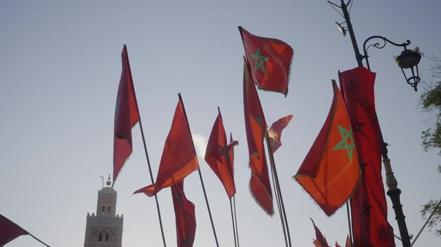 Slow motion cinematic shot of multiple Moroccan flags waving at night with warm street lights in the historic city of Marrakech, Morocco