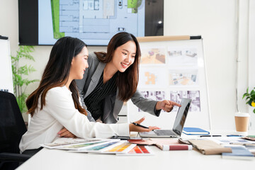 Two creative office employees choosing material and  making interior design on laptop computer in modern office of architectural firm.
