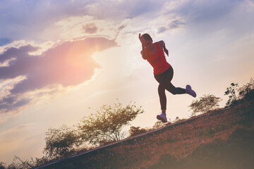 Silhouette of young woman running sprinting on road. Fit runner fitness runner during outdoor workout with sunset background