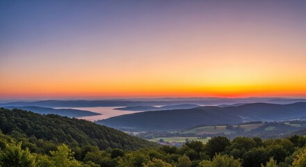 A stunning vista unfolds with layers of forested hills and valleys bathed in the warm glow of a sunrise or sunset, creating a serene and picturesque landscape scene.