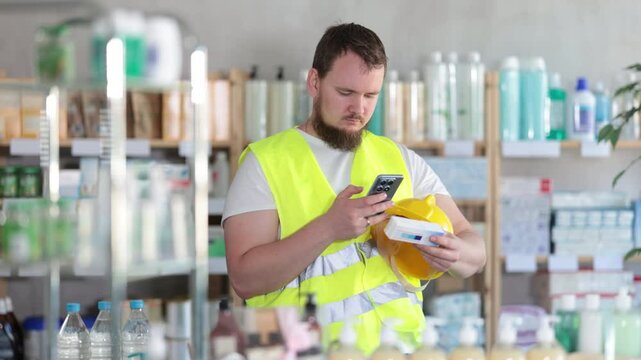Young man builder in uniform scanning qr code for box of ointment in pharmacy