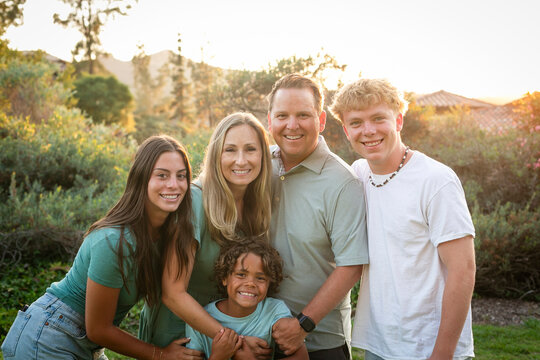 A beautiful diverse family embrace and smile together outdoors. Fun active lifestyle photo showing family love and bonding