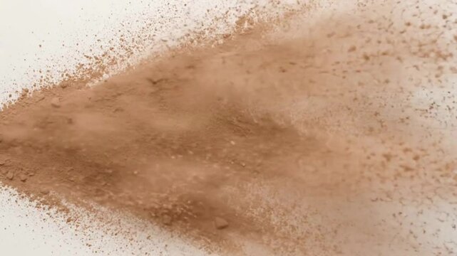 A cloud of tan powder explodes across a white background