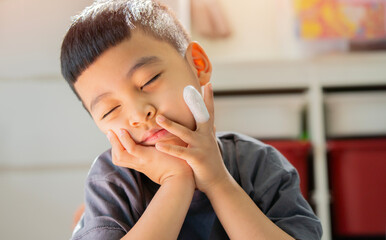 Little funny Asian boy with a wound on his finger lying on the floor, rest chin on hands and...