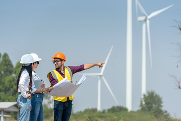 Three people are standing in front of a wind farm