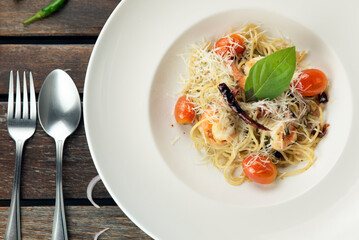 A plate of spaghetti with shrimp, tomatoes, and basil on a wooden table.