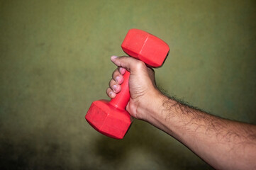 Hand gripping a red dumbbell against vibrant green backdrop, emphasizing strength, fitness, and...