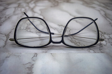 Vintage black square eyeglasses with transparent lenses resting on a marble surface, showcasing...