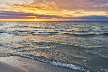 Beautiful landscape of sunset by baltic sea. Golden, shining sun going down and cloudy, colorful sky.	
