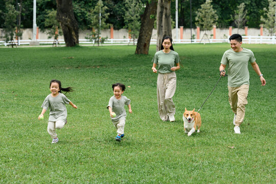 A A cheerful family running together across a green park with their happy corgi - Powered by Adobe
