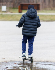 A boy is riding a scooter in the rain