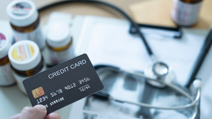 Close-up of hand with black credit card near stethoscope and medicine bottles, hospital billing.