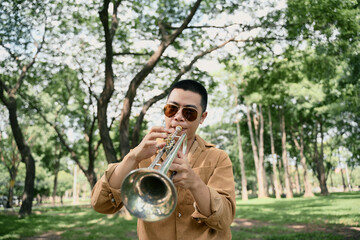 Stylish male artist performing trumpet in a natural setting with trees in the background