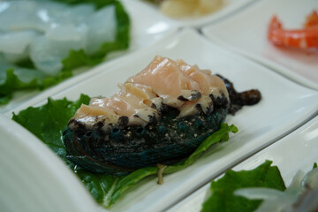 Fresh Abalone Sashimi Slices on White Plate with Green Leaf Garnish