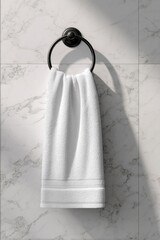 A crisp white hand towel hangs from a matte black circular towel ring mounted on a marble wall, bathed in soft sunlight