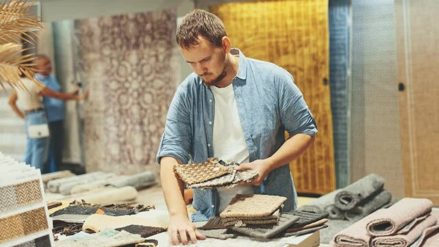 Young man buyer choosing soft carpet samples in building store