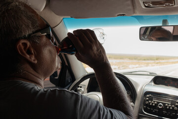 Senior man drinking soda while driving on road trip