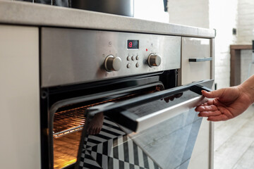 Woman opening a modern oven in a sleek kitchen. The oven interior is illuminated and ready for...