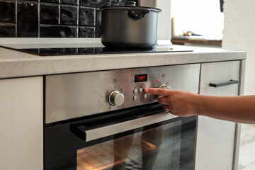 Person setting time or temperature on modern built-in oven using control buttons. Oven is active...