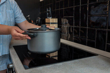 Person placing a pot on a modern induction cooktop in a stylish kitchen with black tile backsplash....