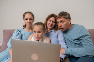 Family Laptop Technology: Family looking at laptop screen, sitting on couch, browsing internet...