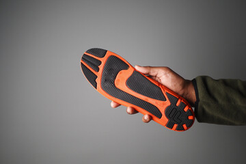 Hand holding an orange and black athletic shoe sole