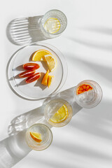 Citrus Infused Water in clear Glasses casting artistic light reflections and palm leaf shadows at sunlight. Summer drink concept, minimal pattern, flavored water with yellow red slices of fruit