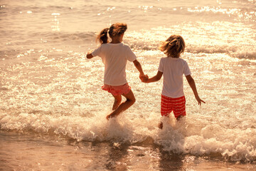 Activity on the beach in summer. A happy little girl and a little boy jump into the sea on a sunny...