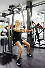 Beautiful and strong athletic woman who using simulator for raising and spreading hands for pumping...