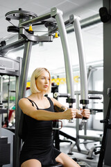 Beautiful and strong athletic woman who using simulator for raising and spreading hands for pumping...