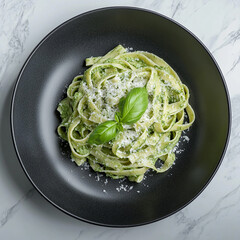 Elegant fettuccine al pesto dish presented on a modern black plate with fresh basil leaf garnish.