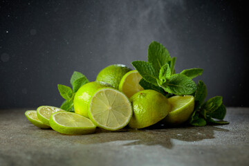 Lime slices and fresh mint branches on a stone table.