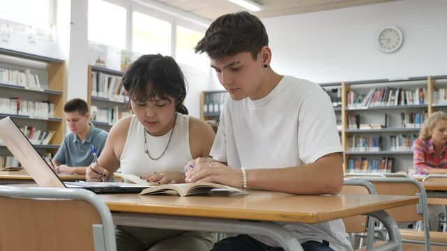 Asian schoolgirl, studying with a classmate guy in the school library on a laptop and making notes in a copybook, preparing for lessons. . High quality 4k footage