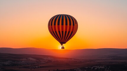 Naklejka premium A vibrant hot air balloon ascends at sunrise, casting a warm glow over a picturesque landscape of rolling hills and valleys