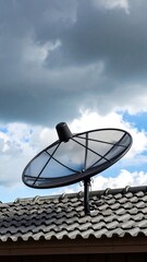 Satellite dish on a tiled roof against a cloudy sky