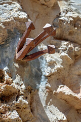 Rusted square-head nails jut from rough stone, casting shadows under harsh sunlight. The scene...