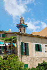Mediterranean stone house with green shutters and balcony, lush plants, and a decorative tower with a blue canopy under clear blue sky; tower, architecture;