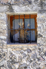 Old stone wall with small barred window, wooden frame, and basket of dried wheat stalks on the...