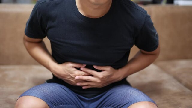 Man sit on sofa feel stomachache touch his belly in the room